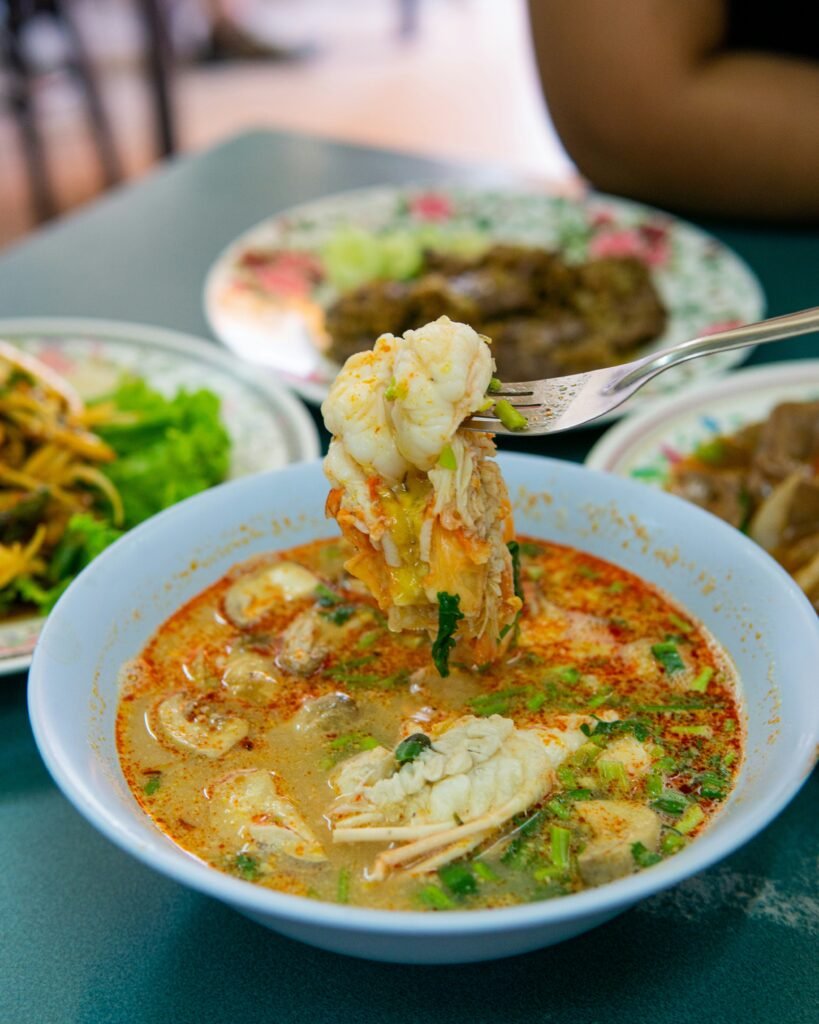 Spicy seafood soup with crab and vegetables at Bistro Hoi An, ELEMENTS, featuring a fork lifting a portion of the dish
