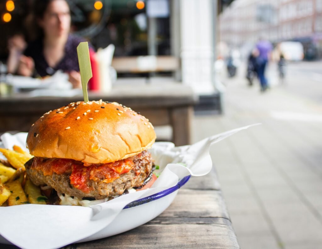 A delicious burger with fries served at a budget-friendly restaurant in London, featuring a juicy patty with spicy sauce, served on a wooden table with a blurred street background.