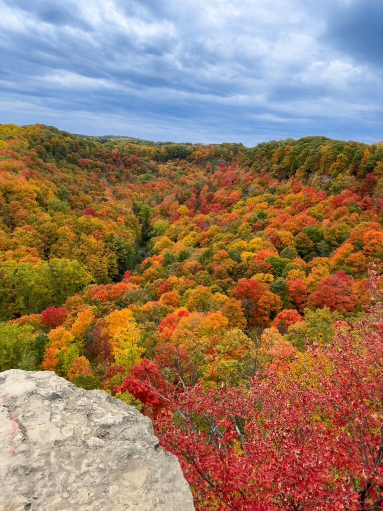 Fall travel 2025 scenic overlook with vibrant autumn foliage in red, orange, and yellow hues under a partly cloudy sky.
