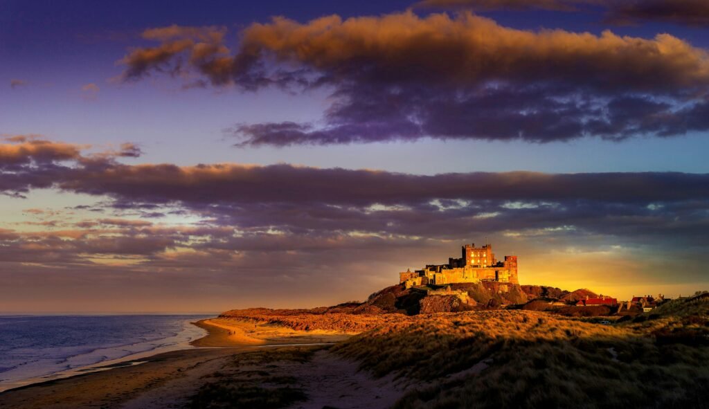Sunset over a coastal castle on a sandy beach with dramatic orange and purple sky.