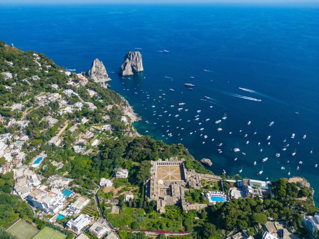 Aerial view of Capri Italy with Faraglioni rocks, Certosa di San Giacomo, and boats on the Tyrrhenian Sea.