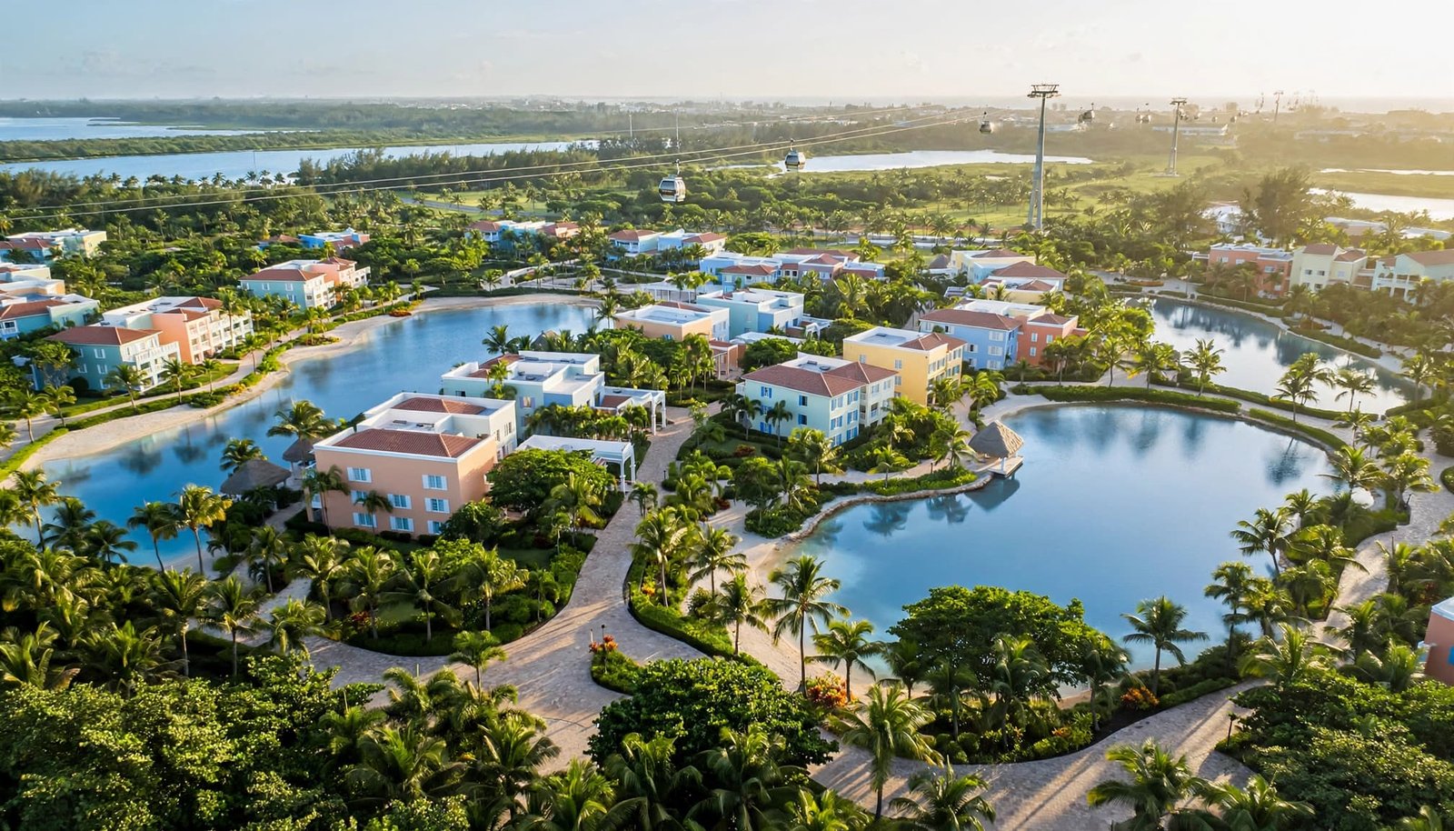 Pastel buildings and palm-lined paths surround a blue lagoon beneath an aerial gondola.
