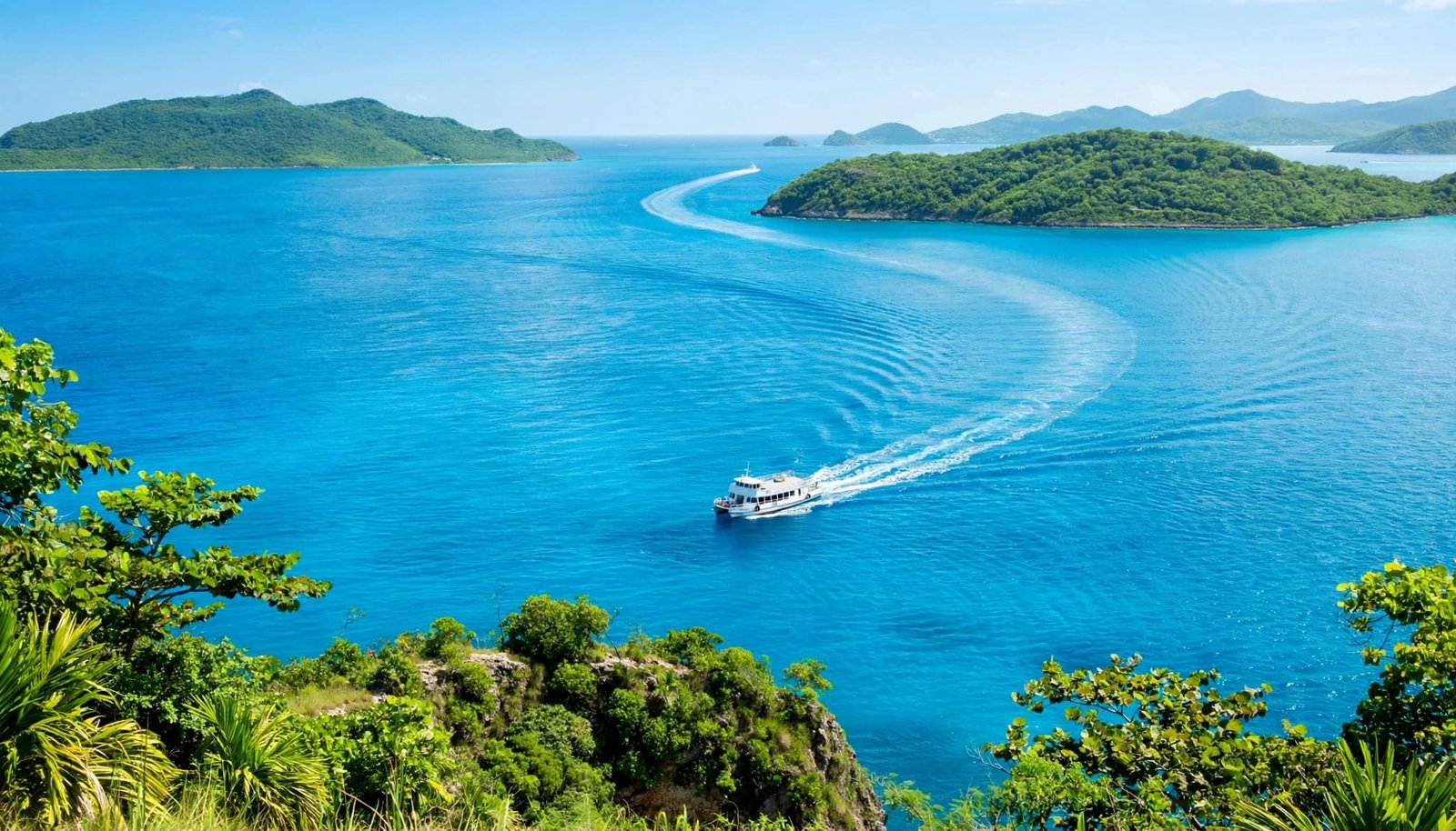 A passenger ferry cruises across bright turquoise water between lush green islands.