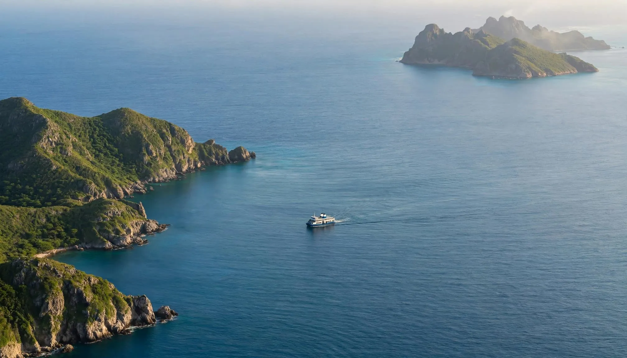 A passenger ferry crosses calm blue water between green Caribbean islands.